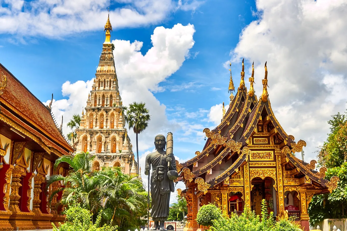 A Thai temple complex with a tiered chedi and a standing Buddha